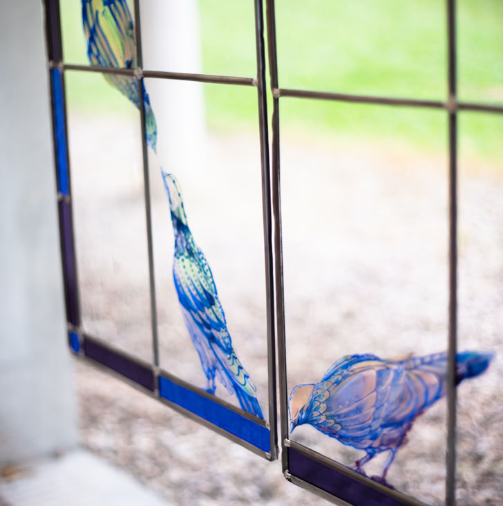 Stained glass window with blue bird designs, set against a blurred outdoor background.